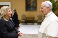 woman with blond hair in a black dress suit conversing with the Pope