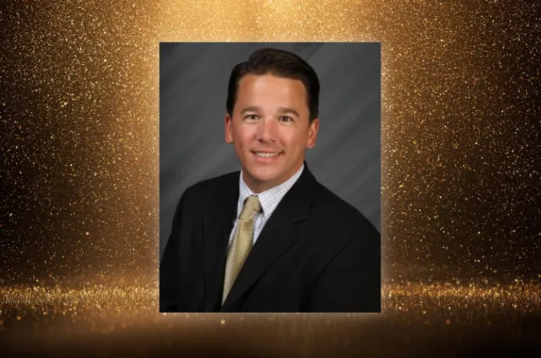 A formal headshot of a man in a suit against a gold glitter background