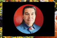 Man with dark hair in a denim shirt against a red background on top of a black square