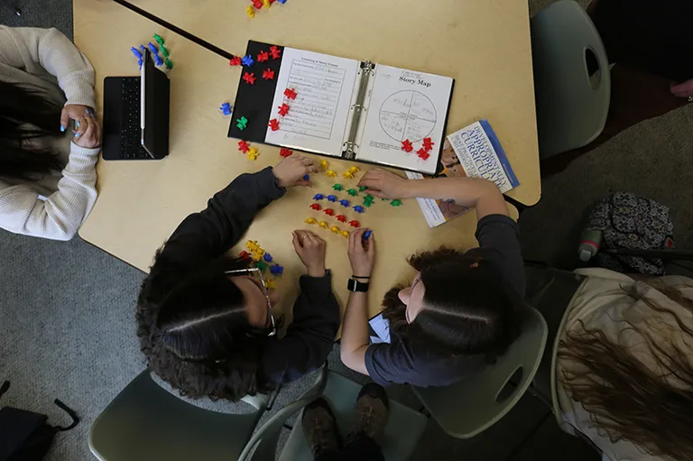 Bird's eye view of two education students sitting at a table. Students rearrange small children's toys on the table