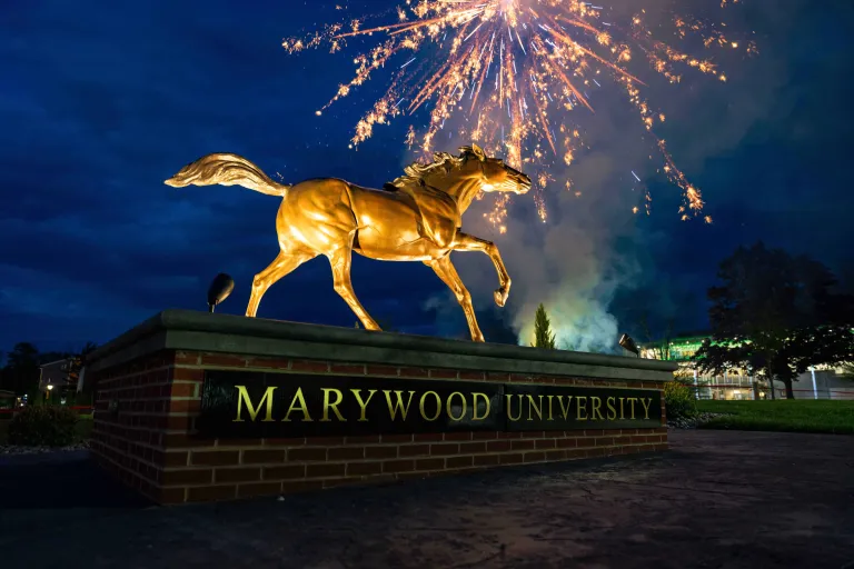 Brass statue of Pacer horse is illuminated at night with fireworks in the sky